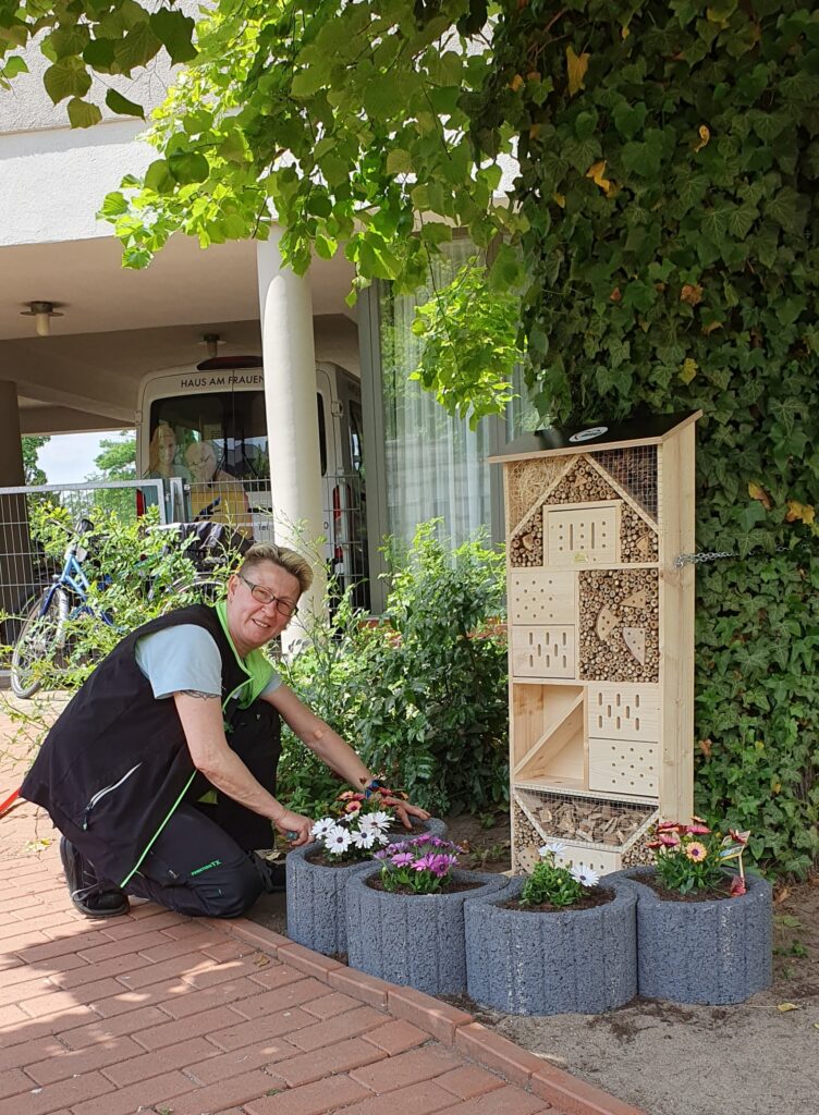 Die Hausmeisterin kniet vor dem neu installierten Insektenhotel